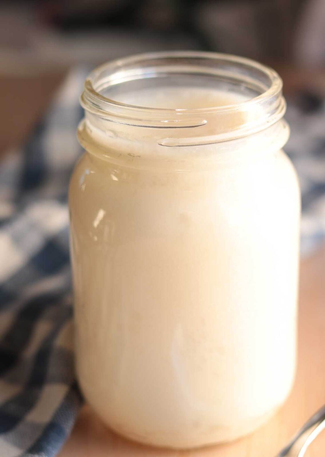 Glass jar filled with creamy white beef tallow on wooden counter.
